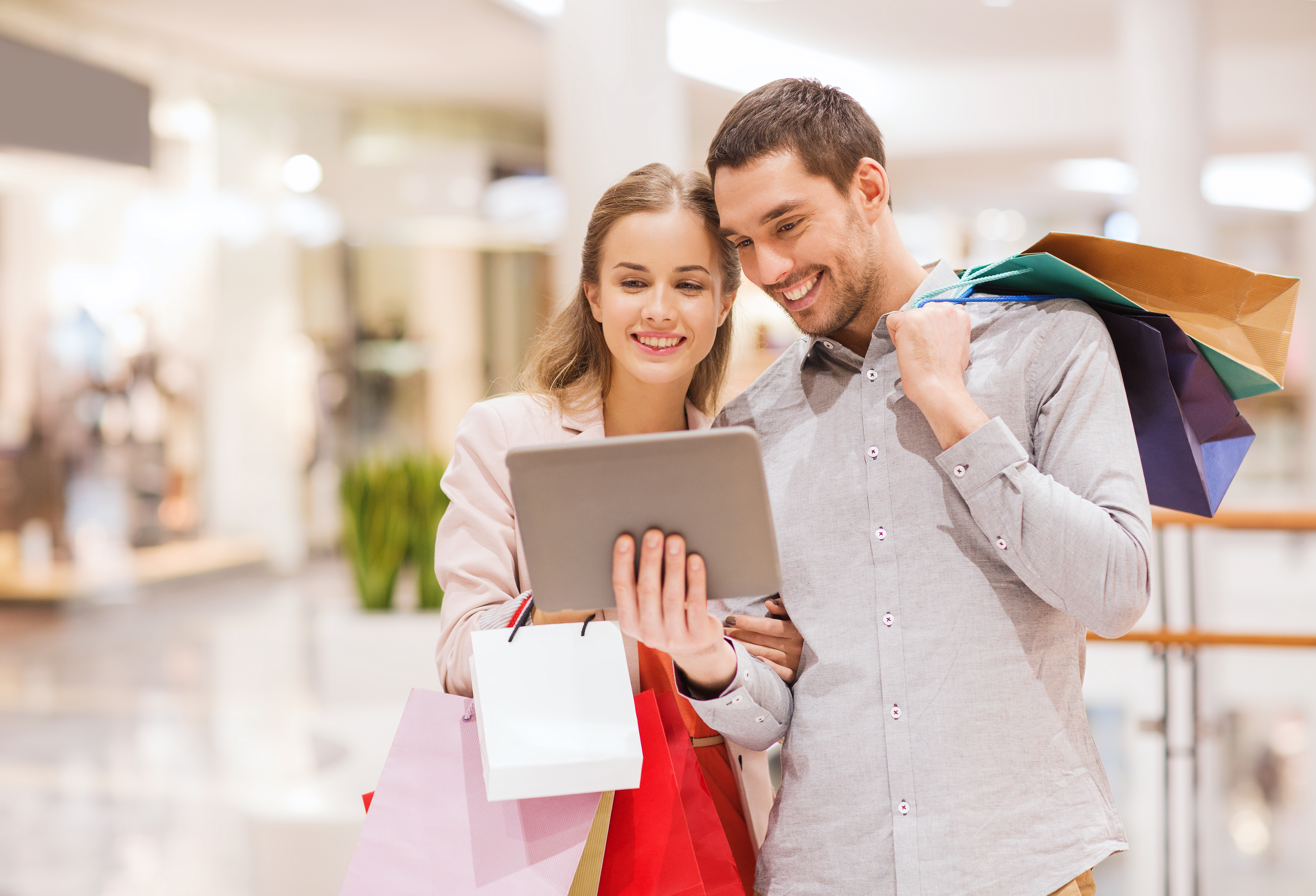 Couple with tablet pc and shopping bags in mall